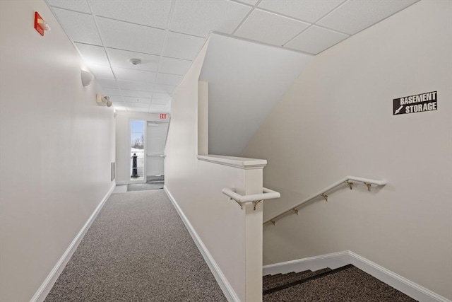 corridor featuring baseboards, a drop ceiling, carpet flooring, and an upstairs landing