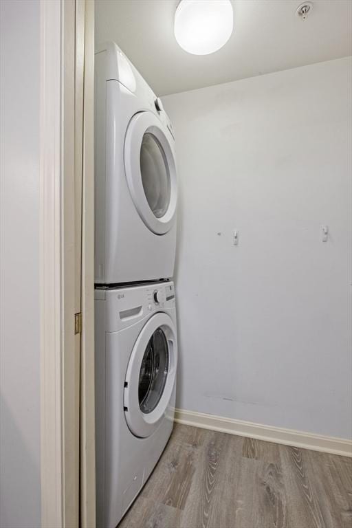 laundry room with stacked washer and dryer, baseboards, laundry area, and wood finished floors