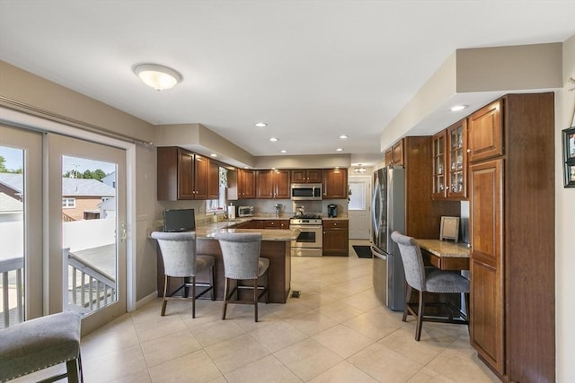 16 Windsor St, Everett, MA 02149 - kitchen featuring appliances with stainless steel finishes, a peninsula, a kitchen breakfast bar, glass insert cabinets, and light tile patterned flooring