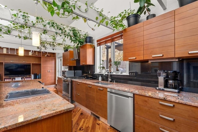 kitchen with sink, wall chimney range hood, light stone counters, light hardwood / wood-style floors, and appliances with stainless steel finishes