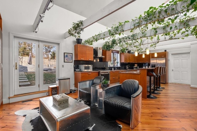 kitchen featuring wall chimney exhaust hood, a breakfast bar, stainless steel appliances, a center island, and light hardwood / wood-style floors