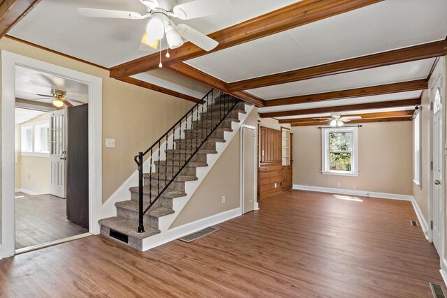 unfurnished living room with a ceiling fan, beamed ceiling, wood finished floors, and stairway