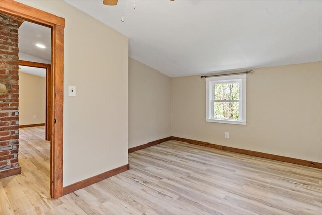 spare room with baseboards, light wood-style flooring, and vaulted ceiling