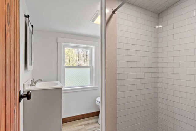 full bathroom with a tile shower, vanity, toilet, baseboards, and wood finished floors
