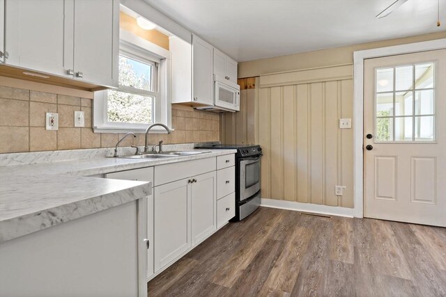 kitchen featuring dark wood finished floors, stainless steel range with electric stovetop, a sink, white cabinets, and white microwave