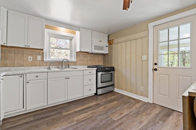 kitchen featuring backsplash, electric range, a sink, white microwave, and white cabinetry