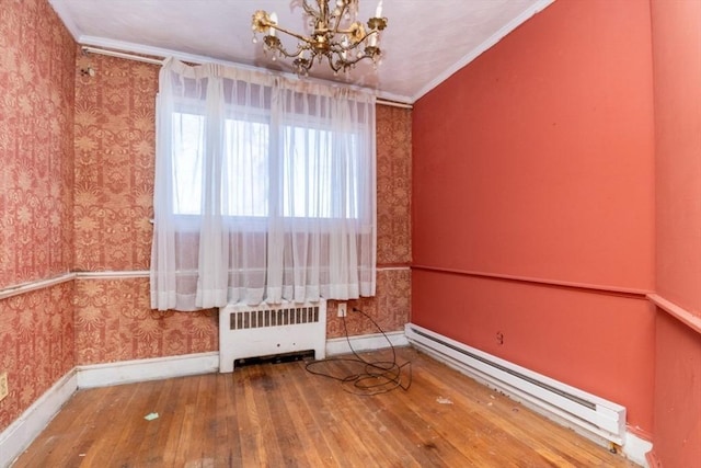 empty room featuring wood-type flooring, radiator heating unit, a baseboard heating unit, ornamental molding, and a chandelier