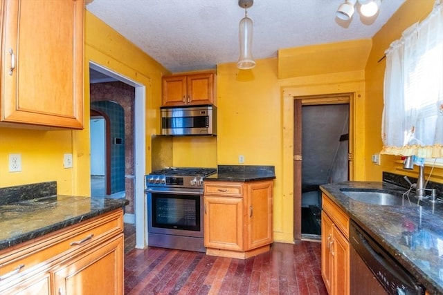 kitchen with a textured ceiling, sink, decorative light fixtures, dark wood-type flooring, and stainless steel appliances