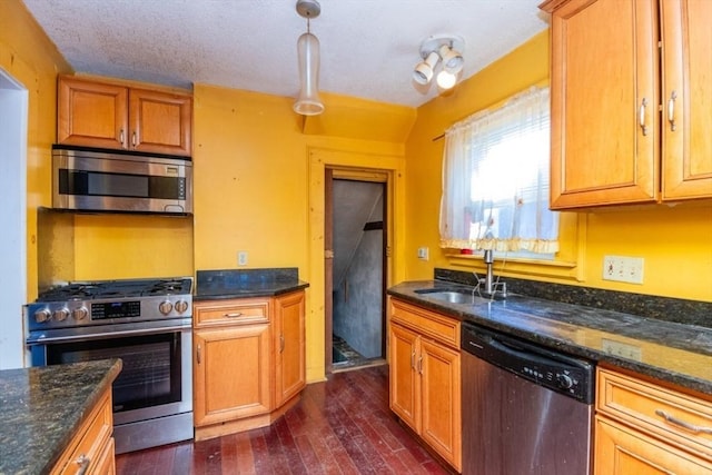 kitchen featuring appliances with stainless steel finishes, decorative light fixtures, dark stone countertops, sink, and dark hardwood / wood-style floors