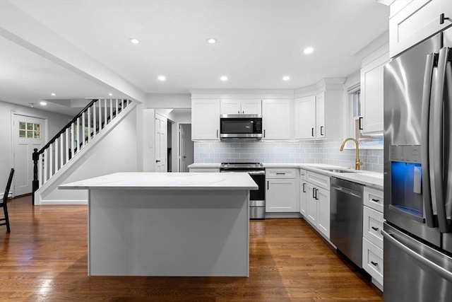 kitchen featuring stainless steel appliances, a sink, a center island, backsplash, and white cabinets