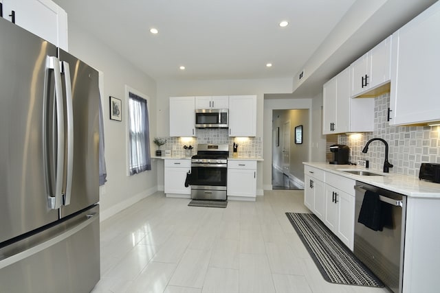 kitchen with stainless steel appliances, sink, light stone countertops, white cabinets, and decorative backsplash