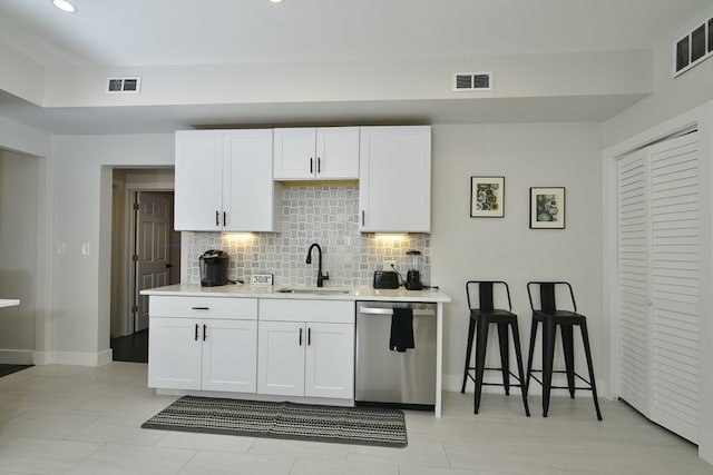 kitchen featuring tasteful backsplash, white cabinetry, light tile patterned floors, sink, and dishwasher