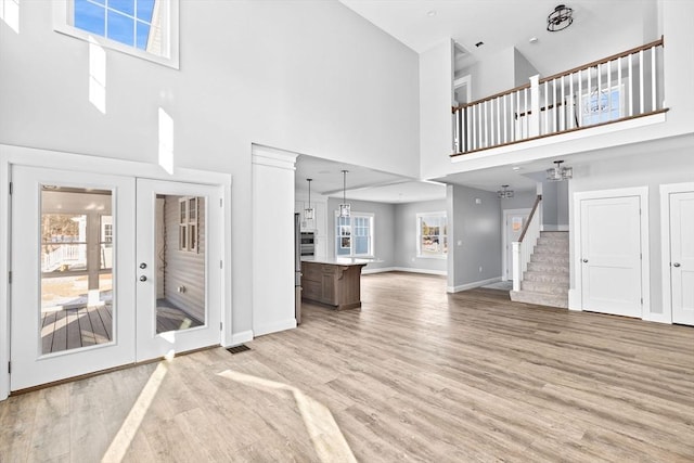 unfurnished living room featuring a high ceiling, light hardwood / wood-style floors, and french doors