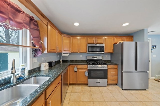 kitchen with stainless steel appliances, light tile patterned flooring, sink, and dark stone countertops