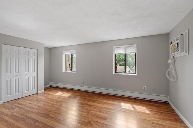 5 Washington St Unit D2, Reading, MA 01867 - unfurnished bedroom featuring a baseboard heating unit, light wood-type flooring, baseboards, and a wall mounted AC