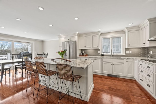 kitchen featuring a breakfast bar, dark wood finished floors, stainless steel fridge, and a sink