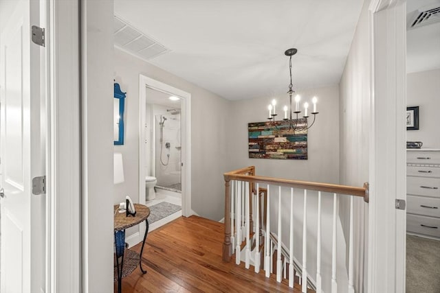 hallway featuring an inviting chandelier, visible vents, wood finished floors, and an upstairs landing