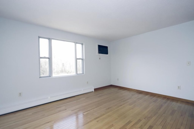 empty room with light wood-style floors, a baseboard radiator, and baseboards