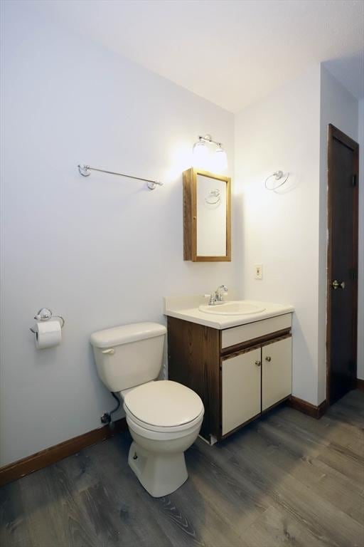 half bathroom featuring toilet, baseboards, wood finished floors, and vanity