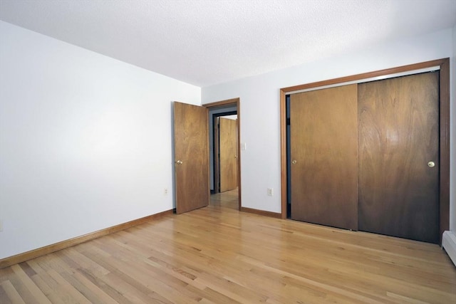 unfurnished bedroom featuring baseboards, a baseboard radiator, a textured ceiling, light wood-type flooring, and a closet