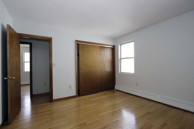 unfurnished bedroom featuring light wood-type flooring, a closet, baseboards, and baseboard heating