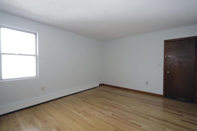 spare room featuring a baseboard heating unit, baseboards, and light wood-style floors