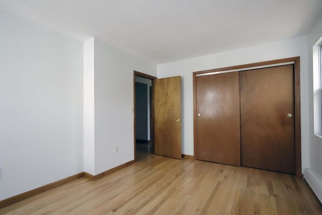 unfurnished bedroom featuring light wood finished floors, baseboard heating, a closet, and baseboards