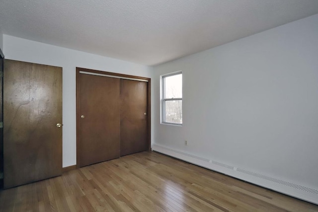 unfurnished bedroom featuring light wood-type flooring and baseboard heating