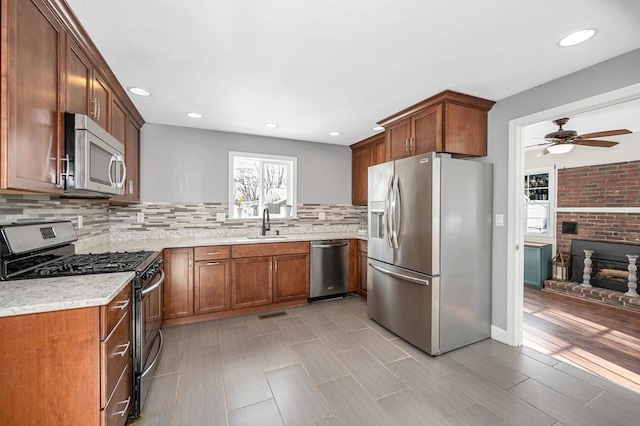 kitchen featuring sink, tasteful backsplash, appliances with stainless steel finishes, ceiling fan, and a fireplace