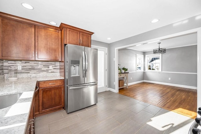 kitchen featuring stainless steel fridge with ice dispenser, light hardwood / wood-style flooring, pendant lighting, light stone countertops, and decorative backsplash