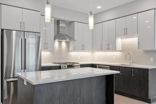 kitchen with wall chimney range hood, appliances with stainless steel finishes, light countertops, and a sink