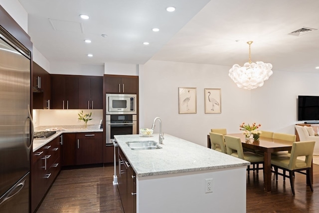 kitchen with dark wood-type flooring, sink, built in appliances, and an island with sink