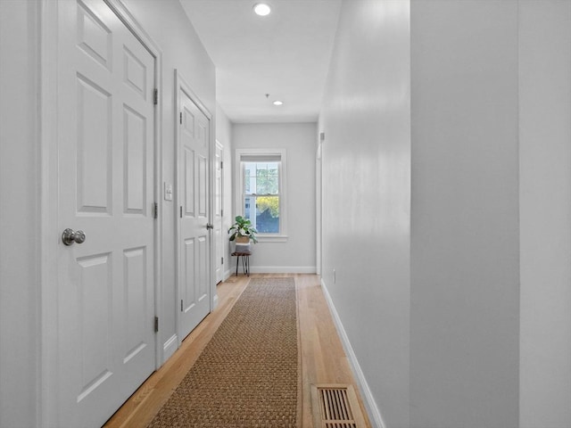 hall featuring light wood-type flooring, visible vents, baseboards, and recessed lighting