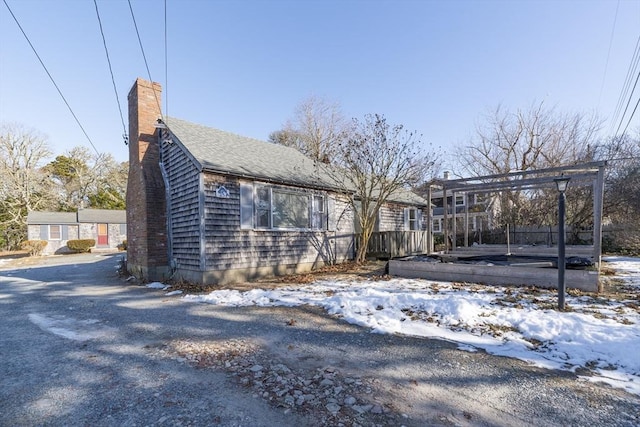 view of snowy exterior with a shingled roof and a chimney