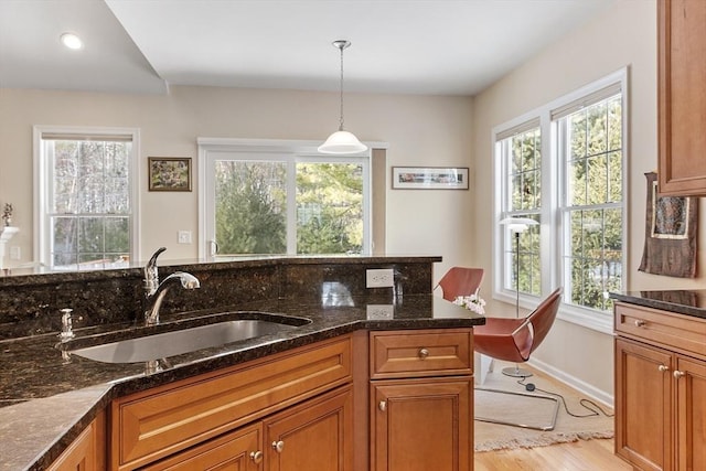 kitchen with dark stone counters, pendant lighting, brown cabinets, and a sink