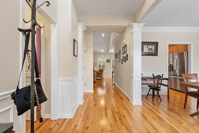 corridor featuring a wainscoted wall, light wood-style flooring, and decorative columns