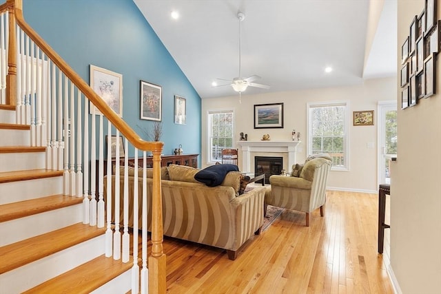 living area with a glass covered fireplace, stairs, light wood-type flooring, high vaulted ceiling, and recessed lighting