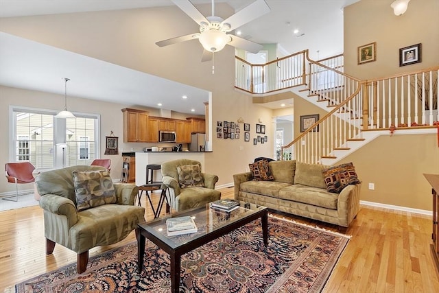 living room with a high ceiling, stairway, light wood-style flooring, and baseboards