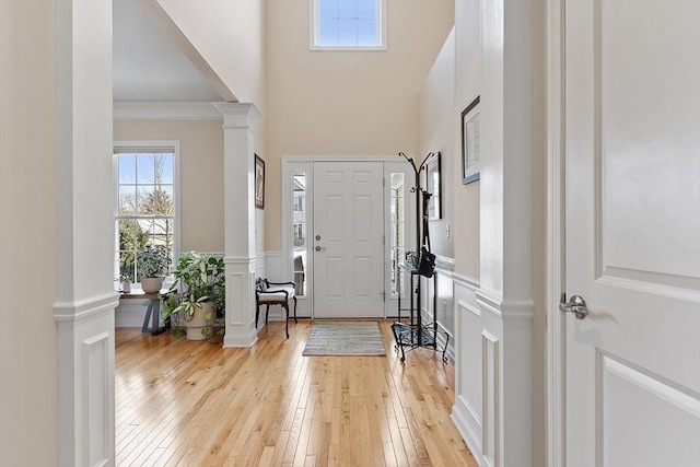 foyer entrance featuring wainscoting, decorative columns, a decorative wall, and light wood finished floors