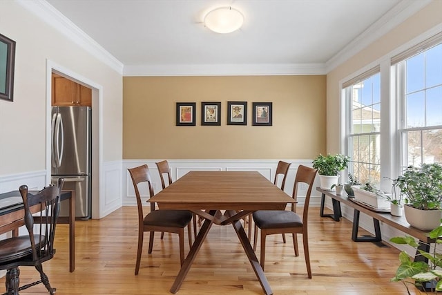 dining area with wainscoting, crown molding, and light wood-style flooring