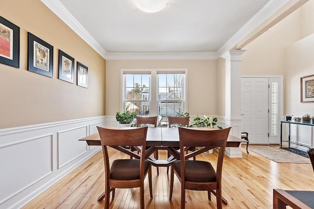 dining room with crown molding, wainscoting, decorative columns, and light wood-style floors