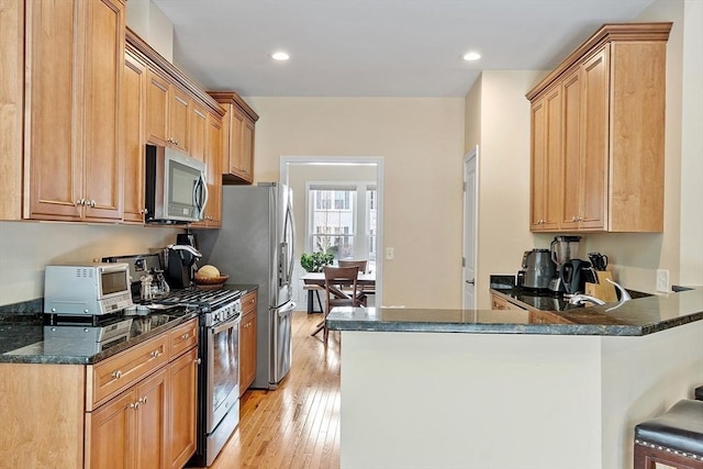 kitchen with appliances with stainless steel finishes, dark stone countertops, a peninsula, and light wood finished floors