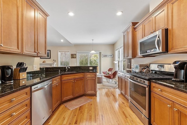 kitchen with dark stone counters, hanging light fixtures, appliances with stainless steel finishes, and brown cabinetry