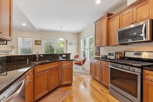 kitchen with pendant lighting, stainless steel appliances, light wood-style flooring, a sink, and dark stone countertops