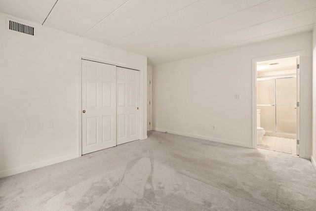 unfurnished bedroom with light carpet, a closet, and ensuite bath