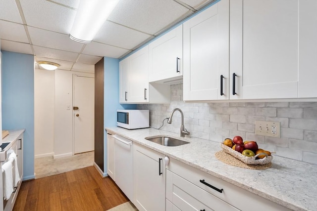 kitchen featuring white cabinetry, a drop ceiling, white appliances, light hardwood / wood-style flooring, and sink