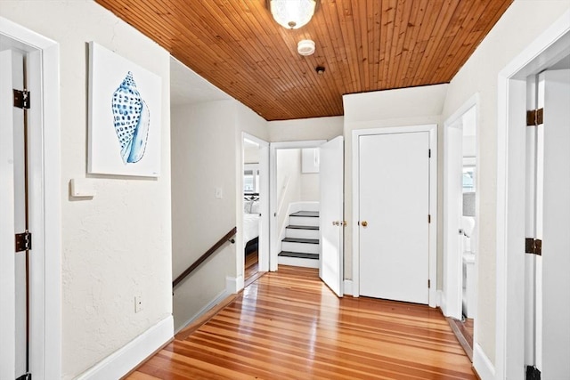 hall featuring stairs, a textured wall, light wood-type flooring, and wooden ceiling