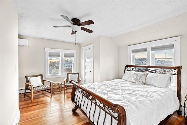 bedroom with a textured ceiling, a baseboard heating unit, wood finished floors, vaulted ceiling, and a wall mounted air conditioner