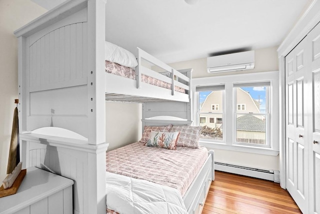 bedroom featuring a baseboard radiator, light wood-style flooring, and a wall mounted air conditioner