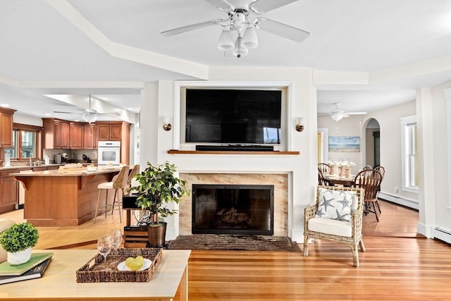 living room featuring light wood finished floors, ceiling fan, a baseboard heating unit, and arched walkways